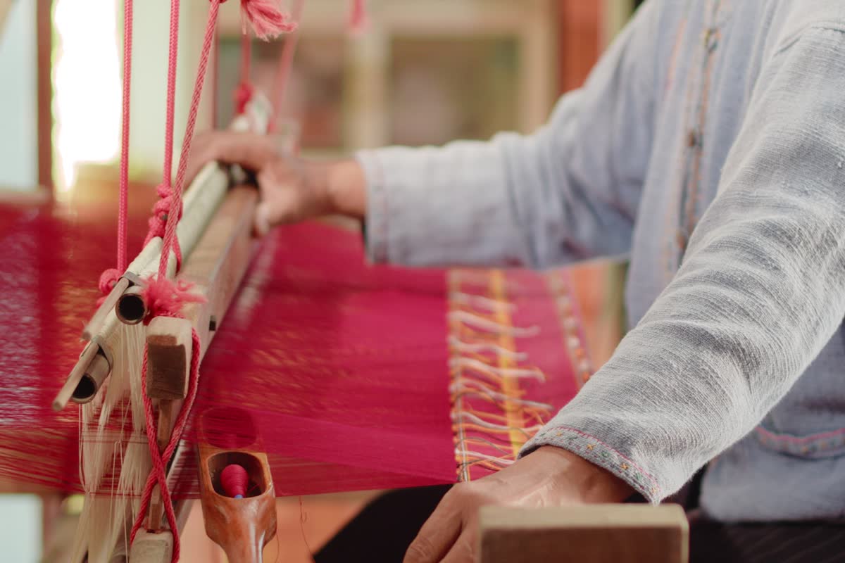 Hands weaving red thread on a wooden loom